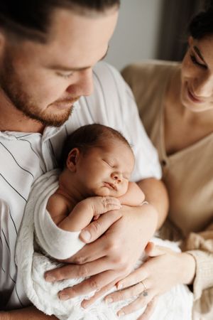 Parents gaze lovingly at their sleeping newborn during intimate indoor portrait session.