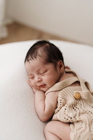 Sleeping newborn baby wearing delicate knit clothing on white background.