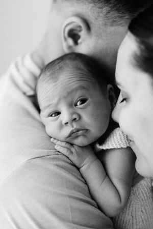 A striking black and white portrait of an alert newborn nestled between parents.