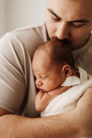 Close-up photos showing tender moments between a parent and sleeping baby wrapped in white fabric.