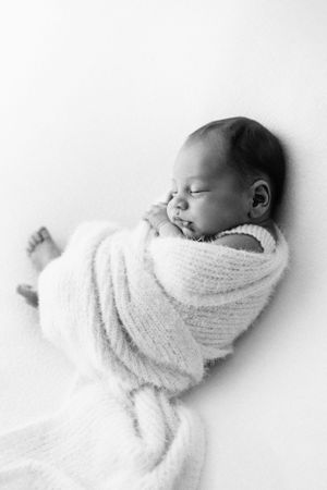 A peaceful black and white portrait of a newborn wrapped in soft knit blanket.
