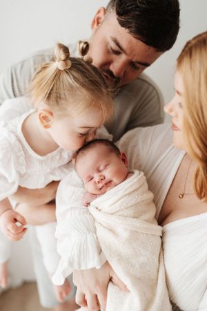 A tender family moment as parents and toddler lovingly gaze at their newborn baby wrapped in white.