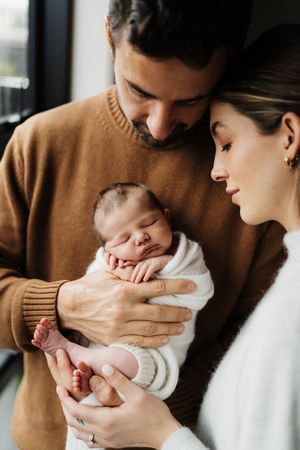 Parents holding and gazing lovingly at their newborn baby in a cozy home setting.