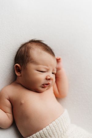 Sleeping newborn baby wrapped in white knit blanket against neutral background.