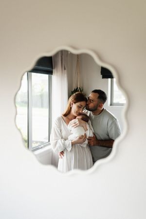 Intimate family portrait reflected in scalloped mirror shows couple with newborn.