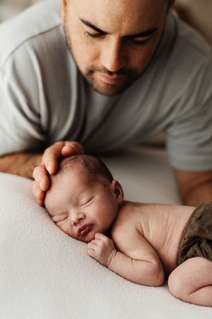 Tender moment between parent and sleeping newborn baby on white surface.