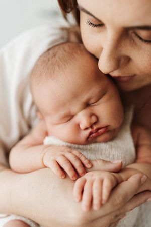 Intimate close-up of sleeping newborn nestled against caregiver in soft natural lighting.