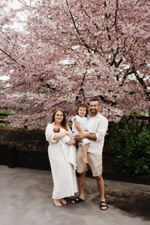 Family of four poses under blooming cherry blossoms in springtime.