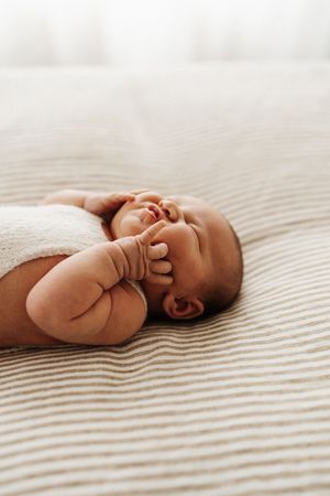 Newborn baby lying on striped bedding while yawning and stretching.