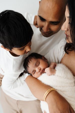 Intimate black and white portraits of parents cradling their newborn baby in white clothing.