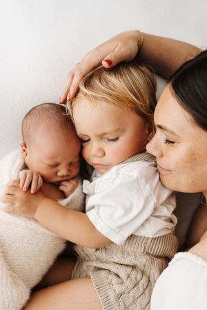 Intimate portraits showing gentle cuddles with a sleeping baby against soft neutral tones.