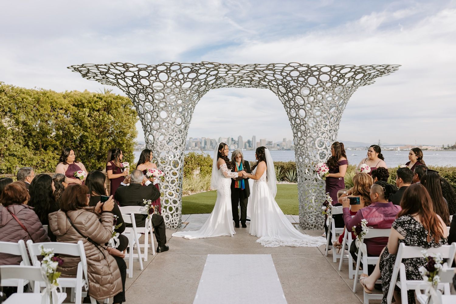 Outdoor wedding ceremony under a modern white latticed arch structure overlooking the ocean with seated guests at Tom Ham's Lighthouse.