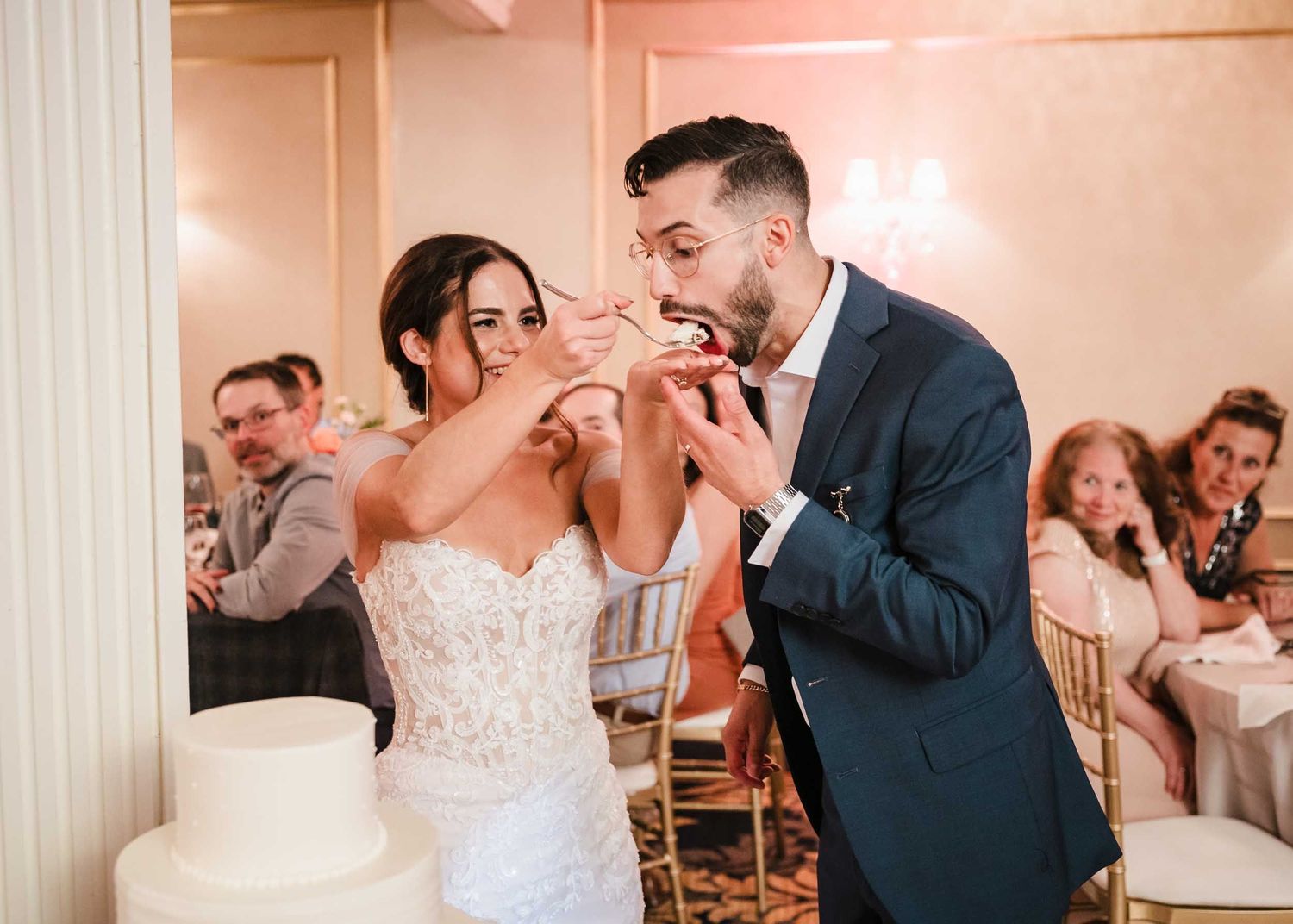 Bride playfully feeds cake to groom during wedding cake cutting at the Lenox Hotel Boston reception