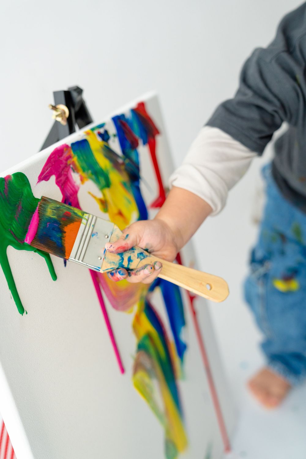 A person's hands holding various art supplies and painting tools, surrounded by vibrant colors.