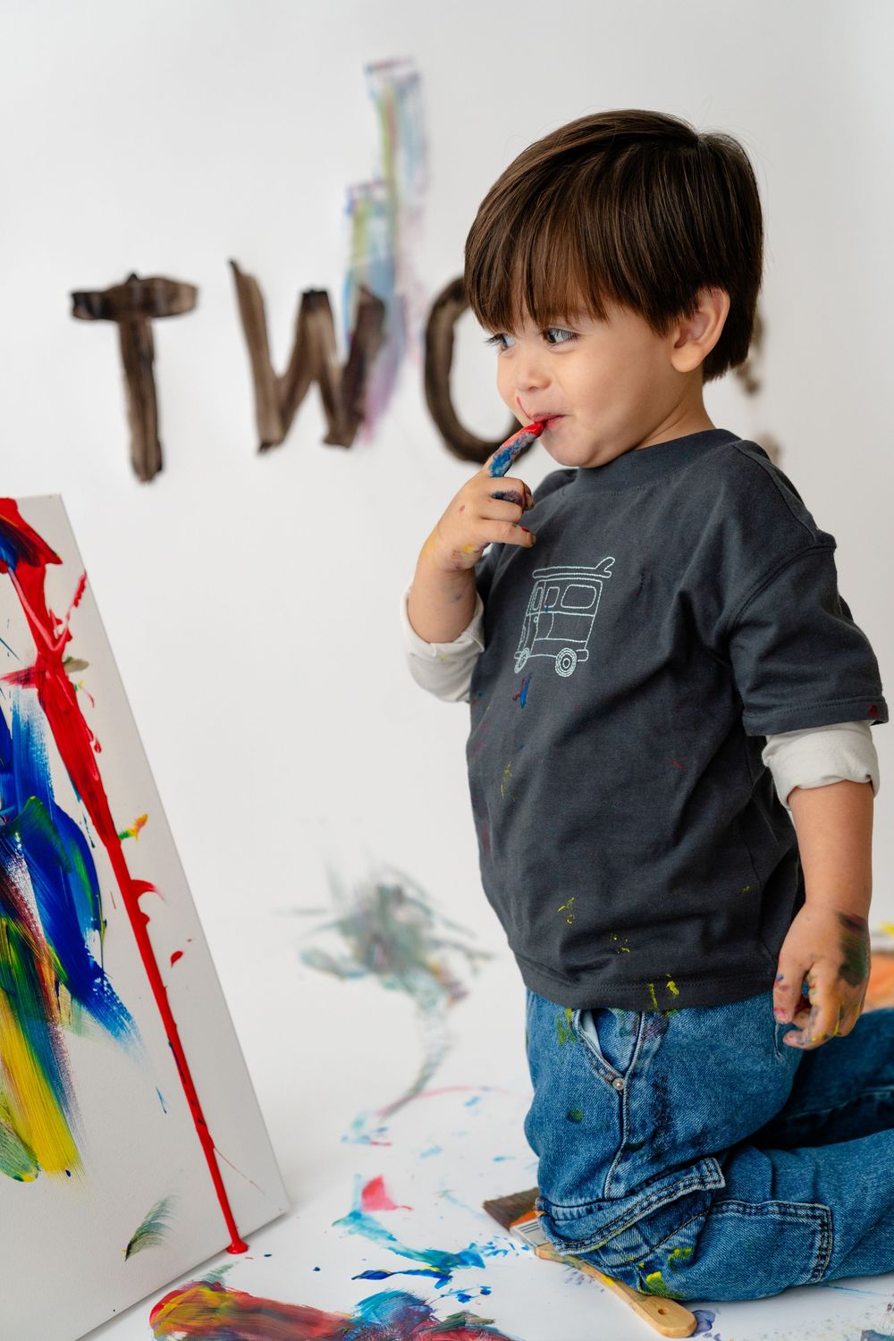A young child sitting on the floor, holding a crayon and creating art on a surface in front of them.