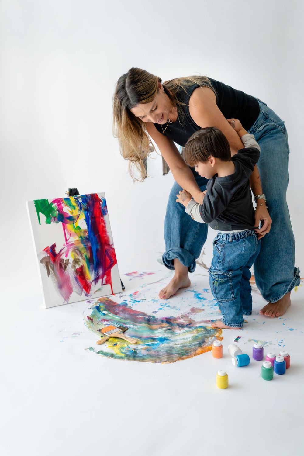 A mother and child painting together on a large canvas filled with vibrant colors and abstract designs.