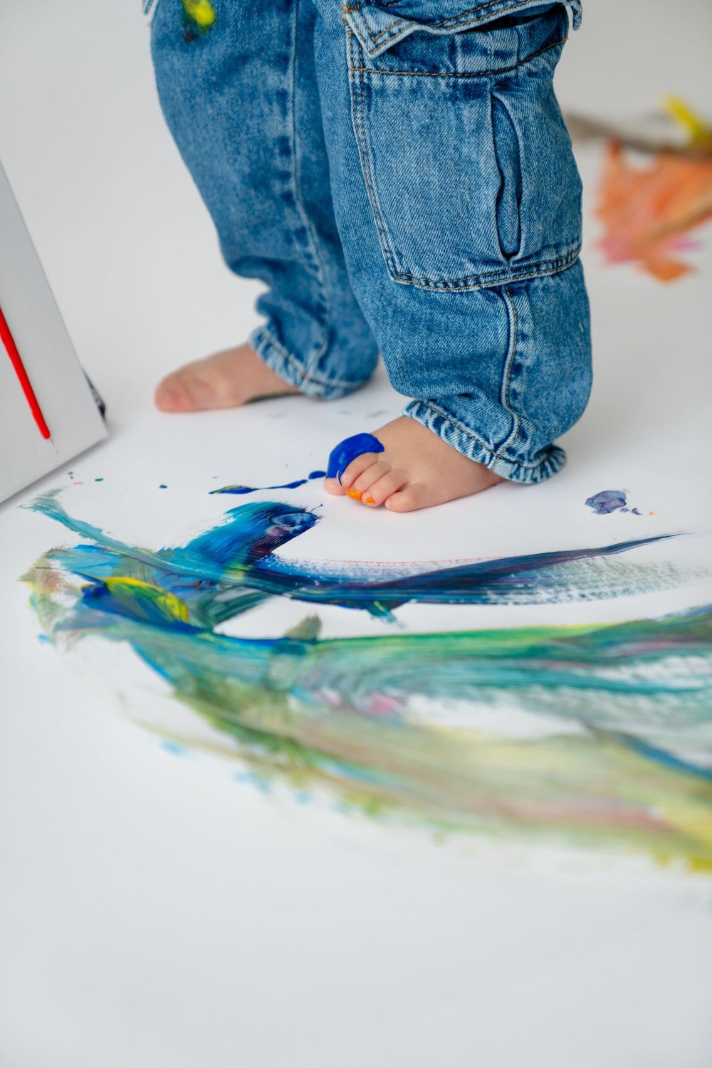A child's feet and hands painting on a white surface, creating colorful abstract art.