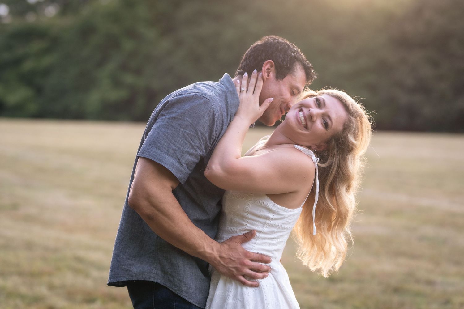 A romantic couple embraces in a sunlit field during a golden hour photo session.