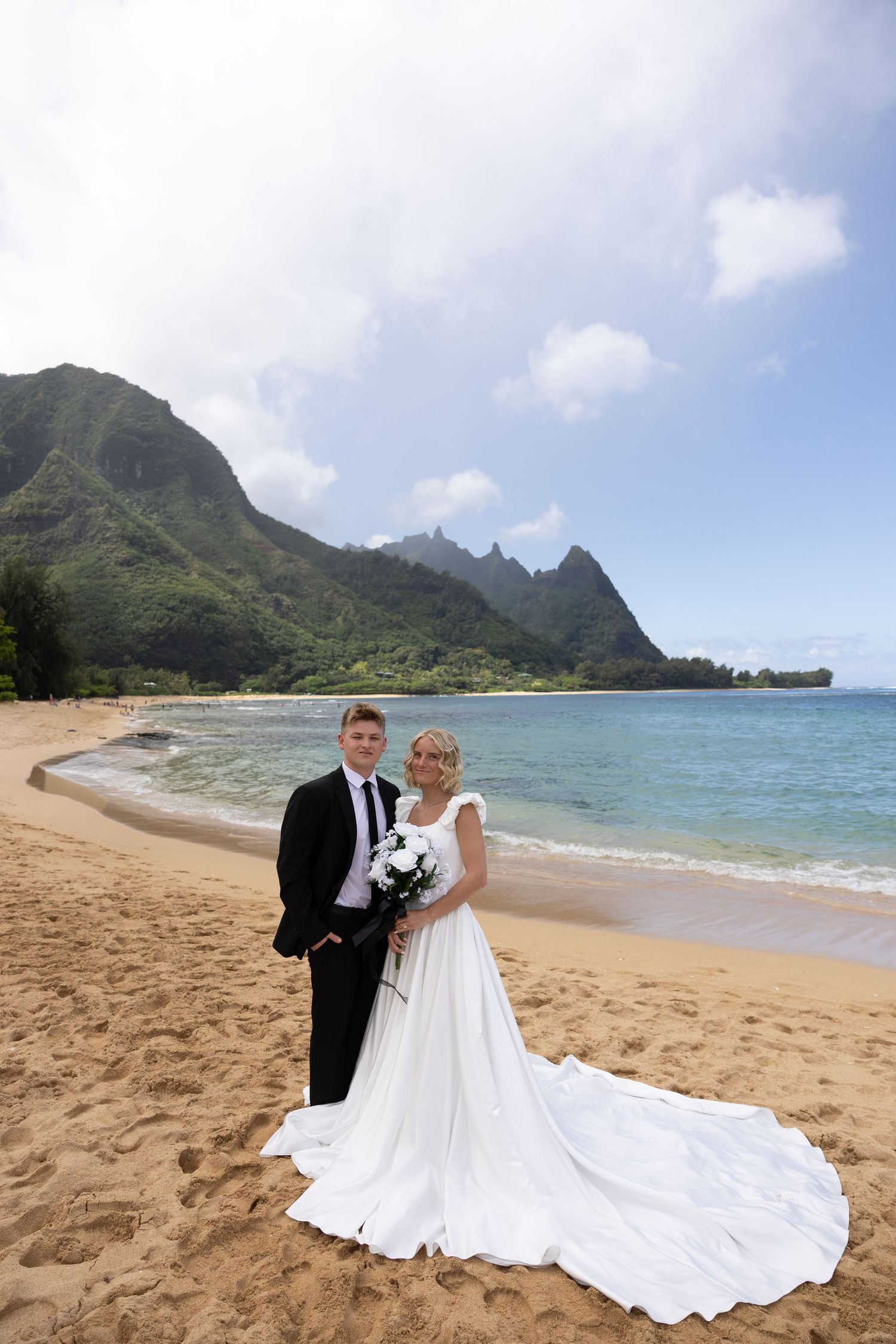 Wedding couple poses on tropical beach with dramatic mountain landscape in Hawaii.