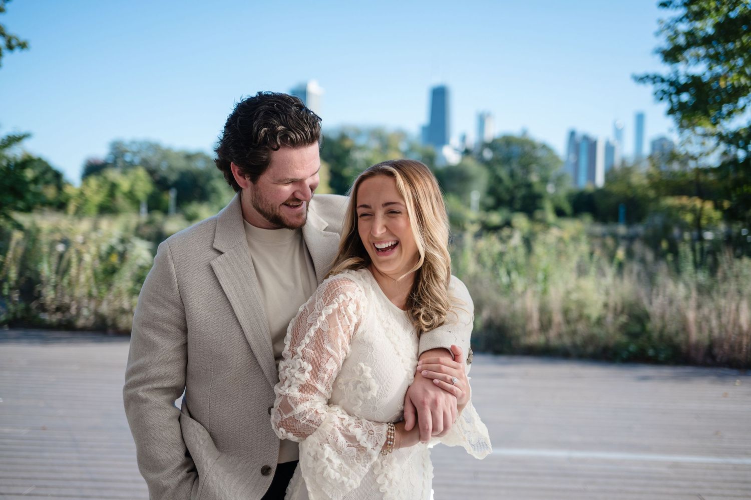 A couple shares a joyful moment together outdoors with city skyline and natural scenery in the background.