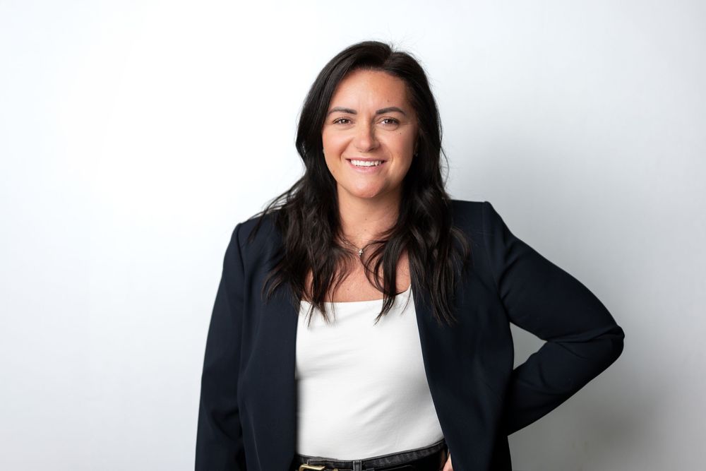 Smiling woman with dark hair in a navy blazer and white top posing with hand on hip in a headshot.