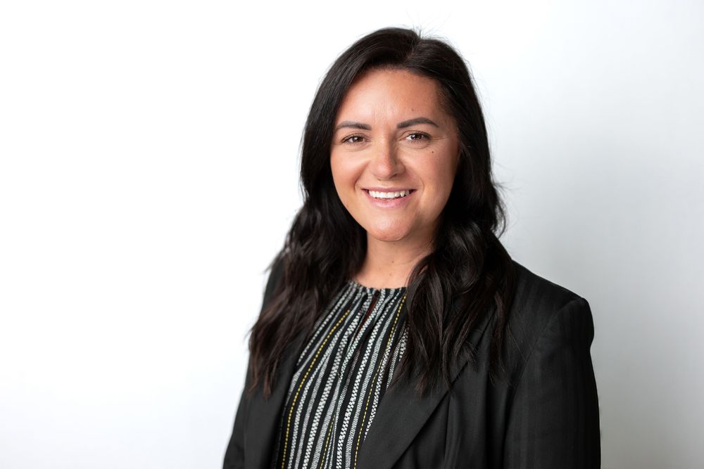 Professional headshot of a dark-haired woman smiling, wearing a black blazer and striped blouse.