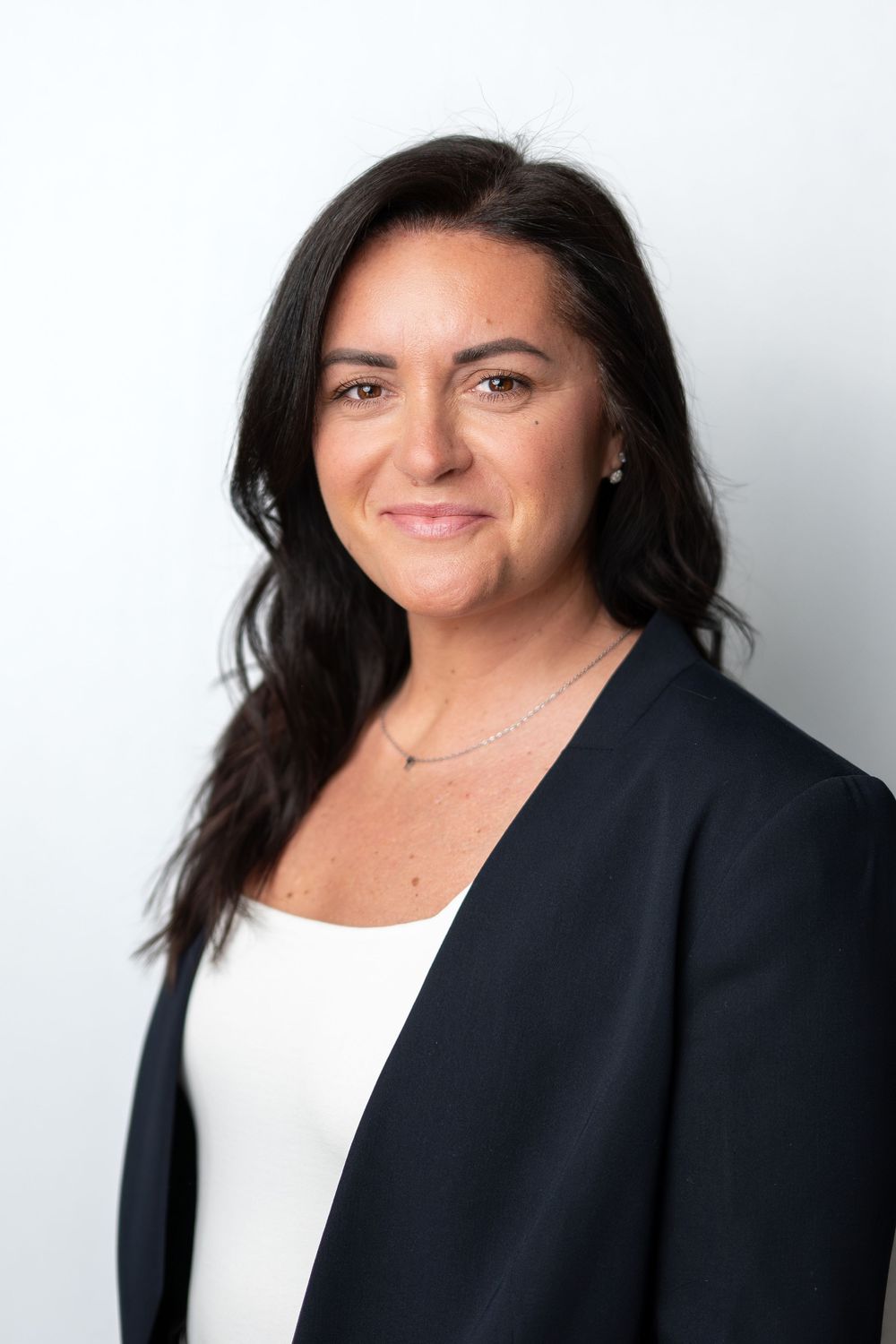 Professional headshot of a woman with dark hair wearing a navy blazer and white top against a white background.