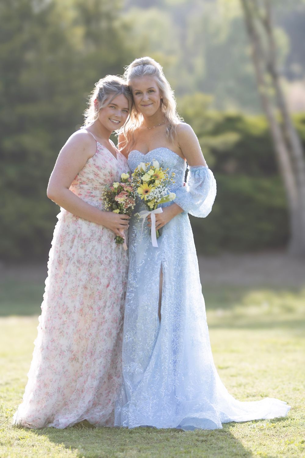 Two people in formal dresses share a joyful moment together outdoors during a wedding celebration.