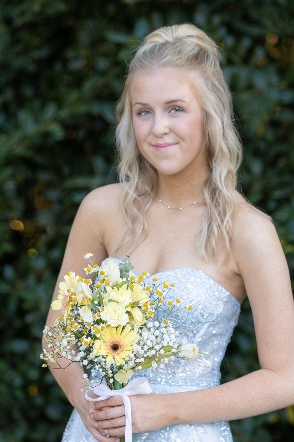 A bride in a white sequined dress holds a rustic bouquet with yellow sunflowers, baby's breath and blue accents.