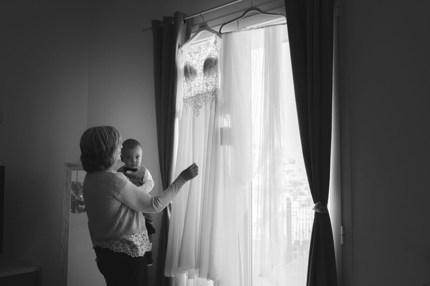 mamma della sposa e figlio degli sposi guardano l'abito appeso alla finestra