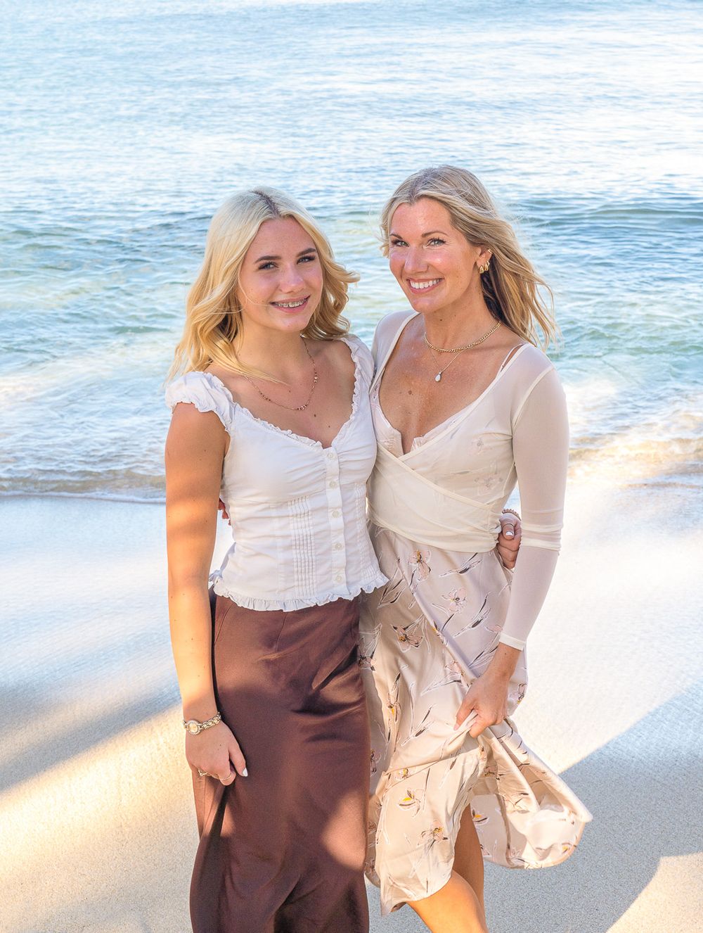 Two friends share joyful moments together on a sunny beach with waves and sand in the background.