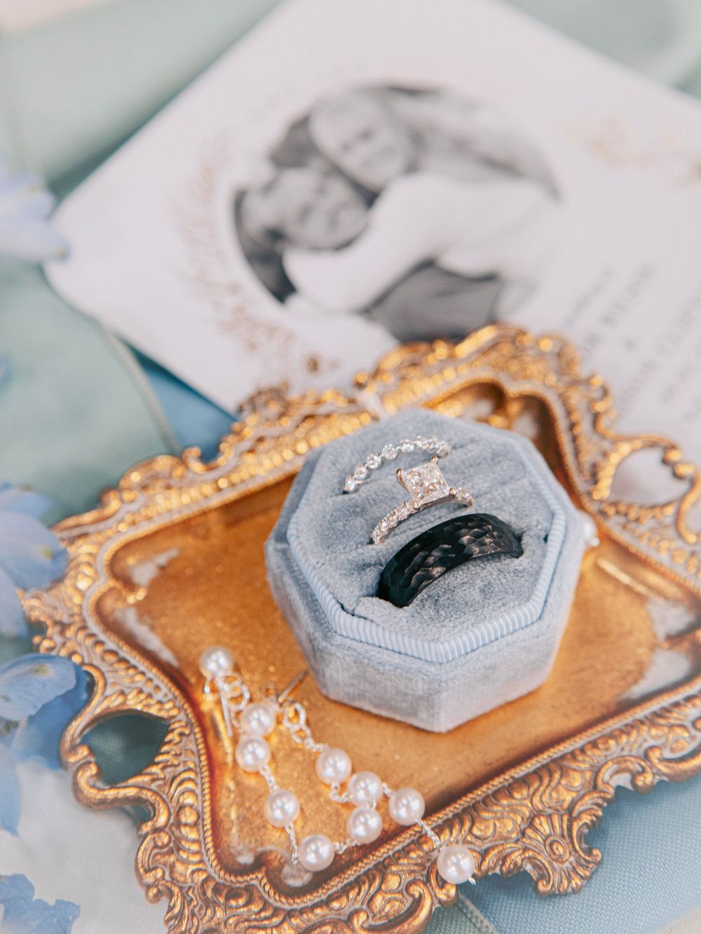 Vintage ornate copper frame displays an elegant gray ring box with pearls scattered around it.