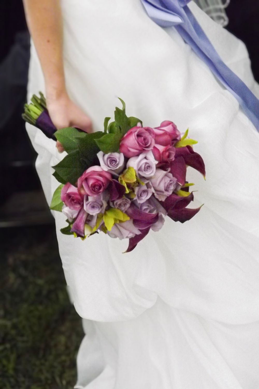 A white wedding dress adorned with a vibrant floral arrangement of purple, pink and yellow blooms along the waistline.