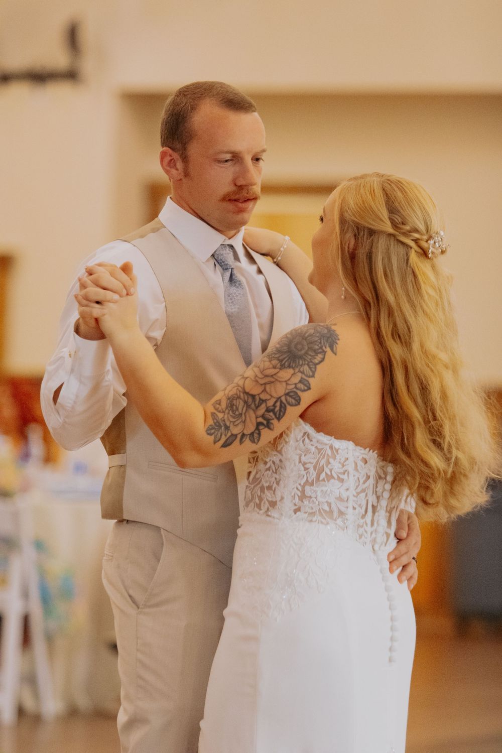 Couple shares their first dance at wedding reception with bride in lace dress and groom in light gray suit.