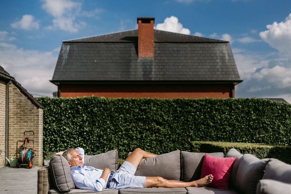 A modern outdoor patio setup with gray cushioned furniture and decorative pillows against a brick wall with climbing vines.