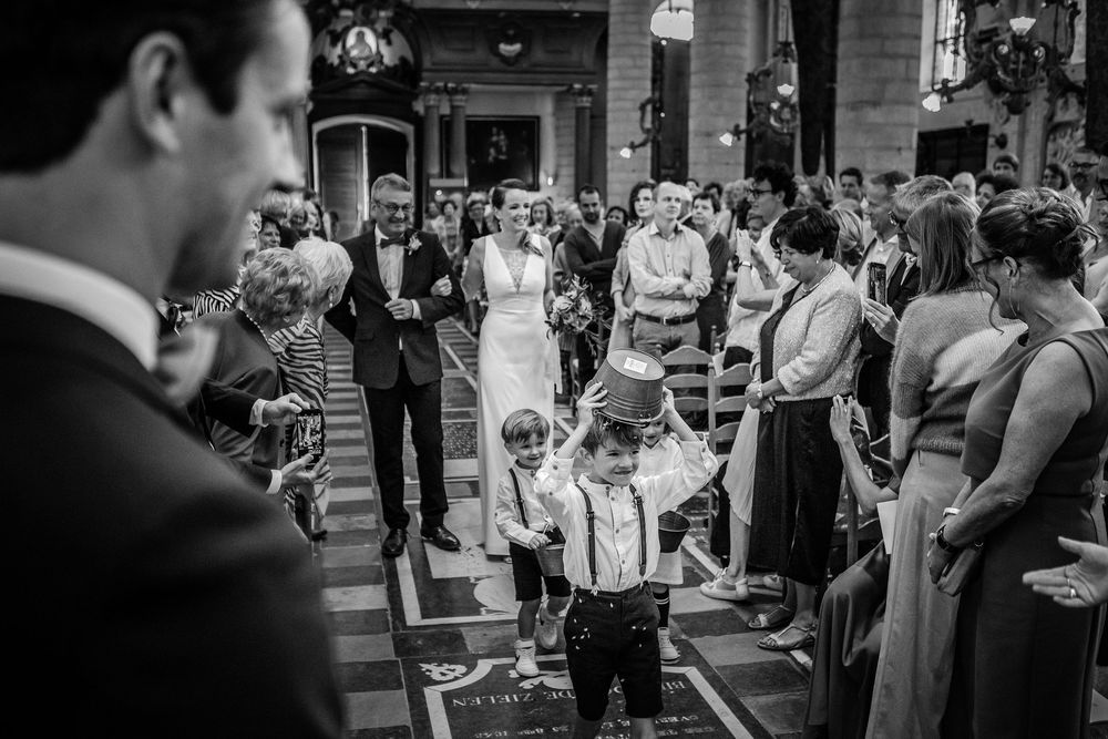 Black and white photo of a young boy in suspenders walking down the church aisle during a wedding ceremony.