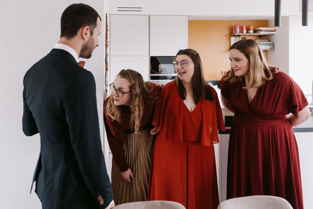 People in coordinating burgundy and brown dresses gather in a bright room for a photoshoot.