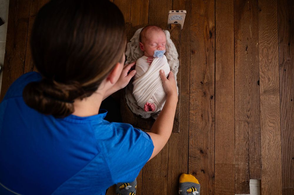 A photographer captures a newborn portrait session against a rustic wooden wall background.