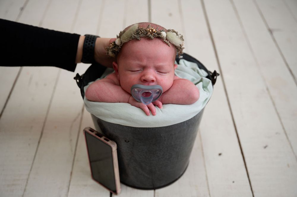 A series of photos showing a newborn baby being photographically posed in a black cooking pot on a white wooden floor.