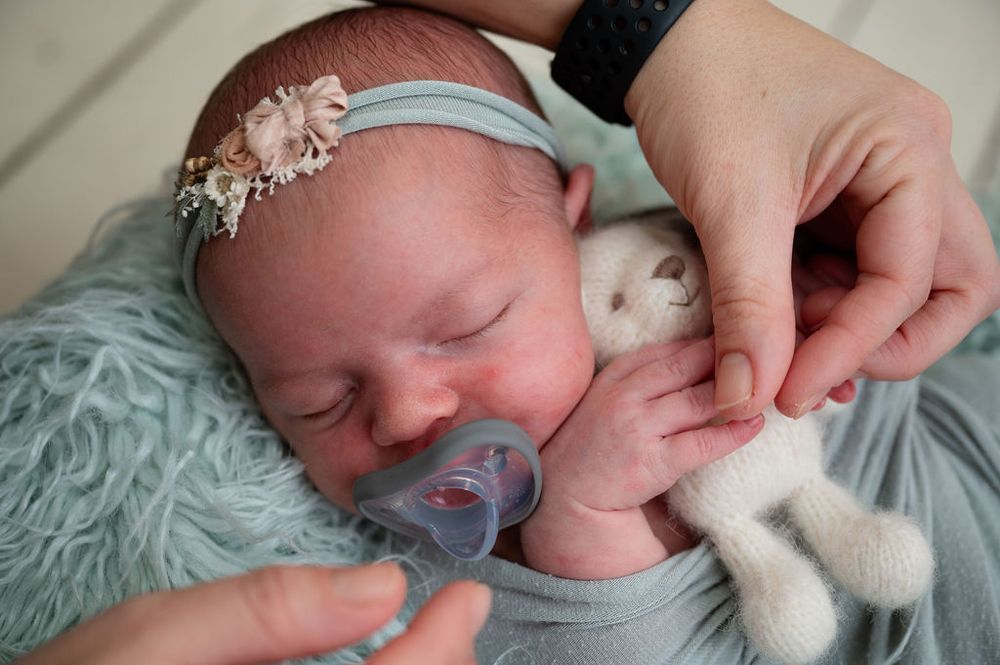 Sleeping newborn baby in soft teal blankets with pacifier and stuffed animal.