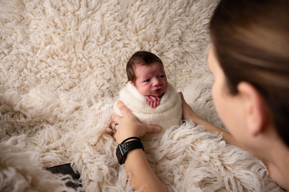 Lifestyle newborn photography session featuring gentle interactions on plush white carpet.