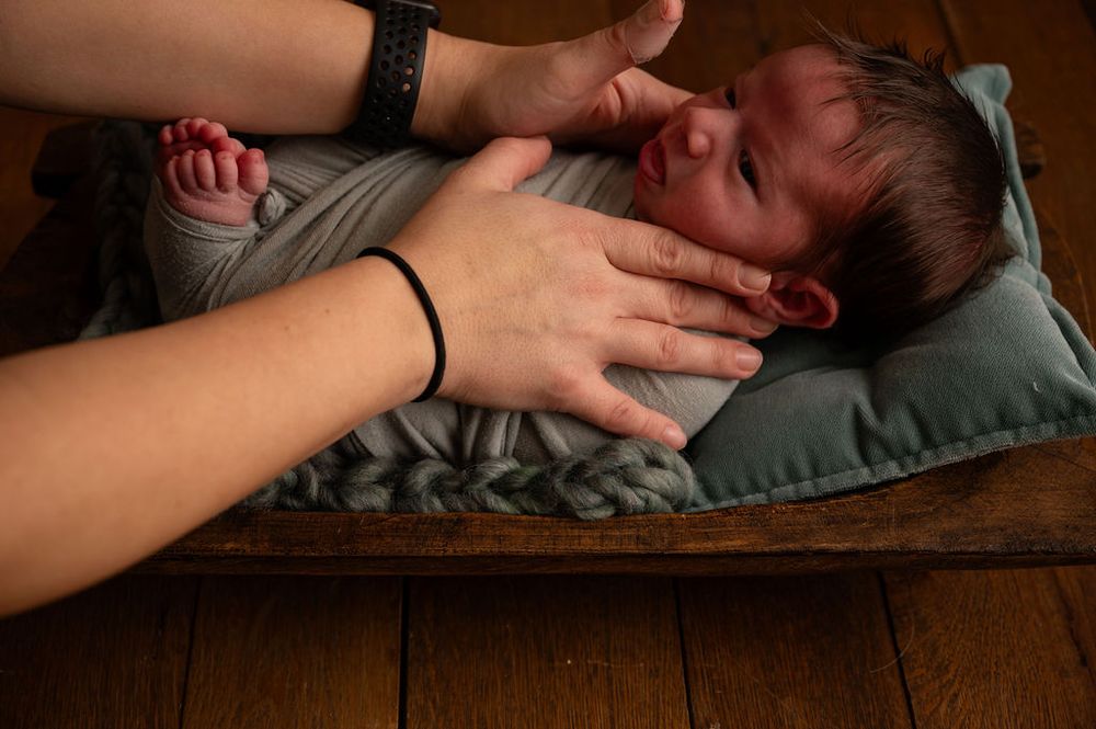 Close-up of hands gently touching a sleeping baby on wooden surface.