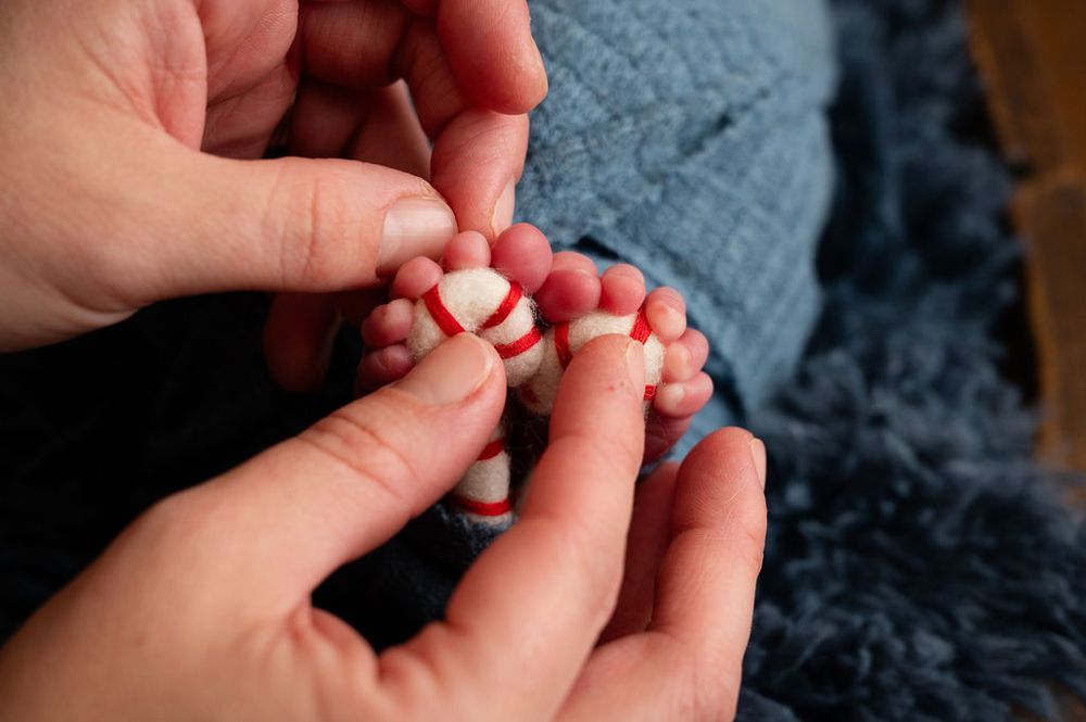 Close-up of gentle hands holding tiny baby feet with red painted toenails.