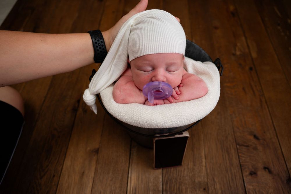 A sleeping newborn baby wearing a white knit hat rests peacefully on a wooden surface.