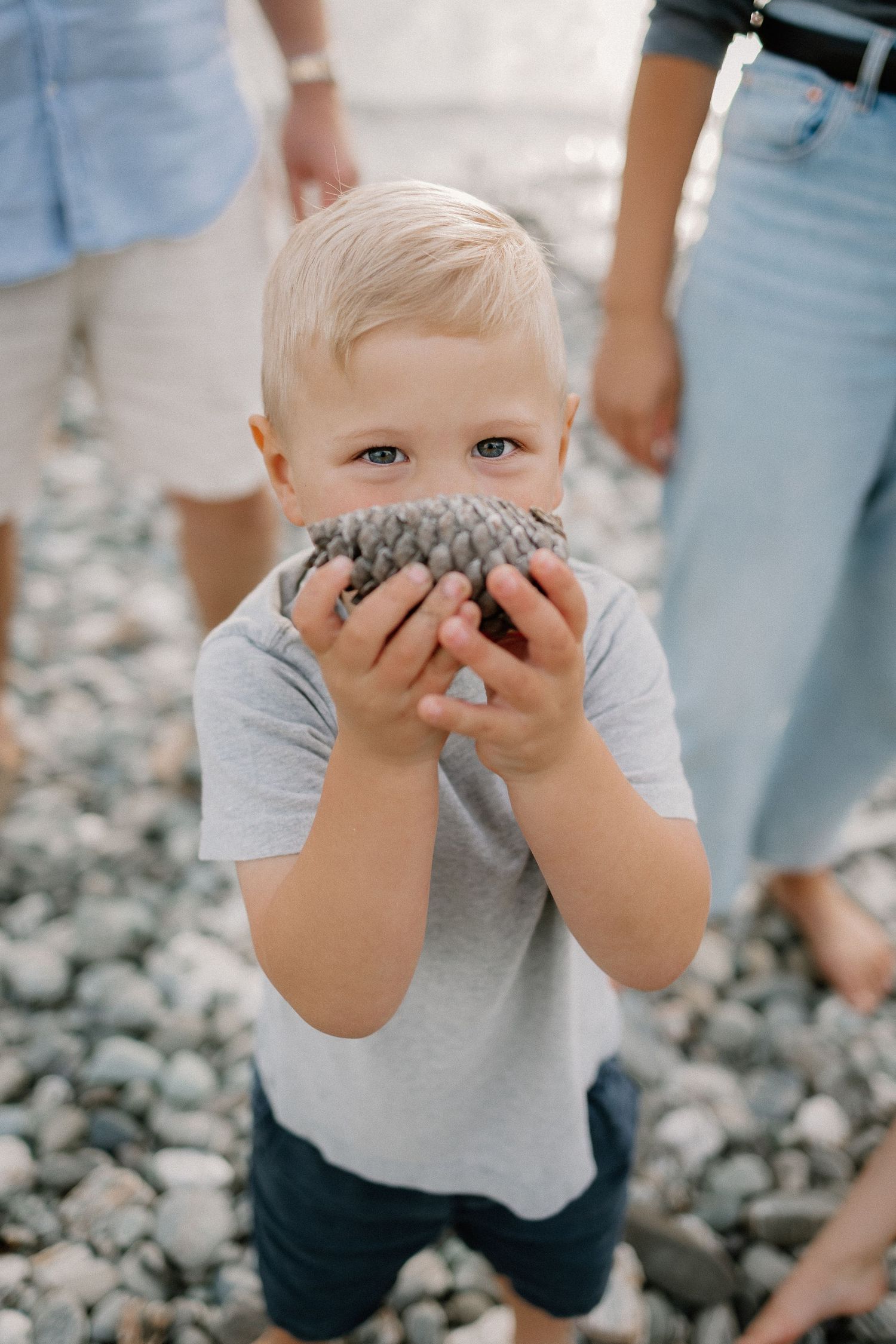 Toddler boy hides from the camera with a pinecone during a family photoshoot at Lake Wakatipu, Homestead Bay in Queenstown.