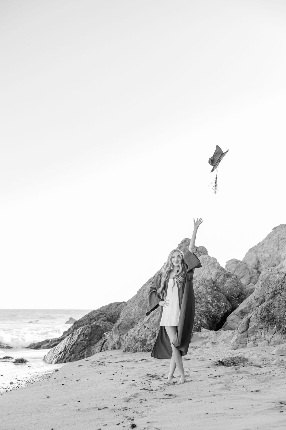 A sequence of four black and white photos showing a person in a dress posing near coastal rocks at the beach.