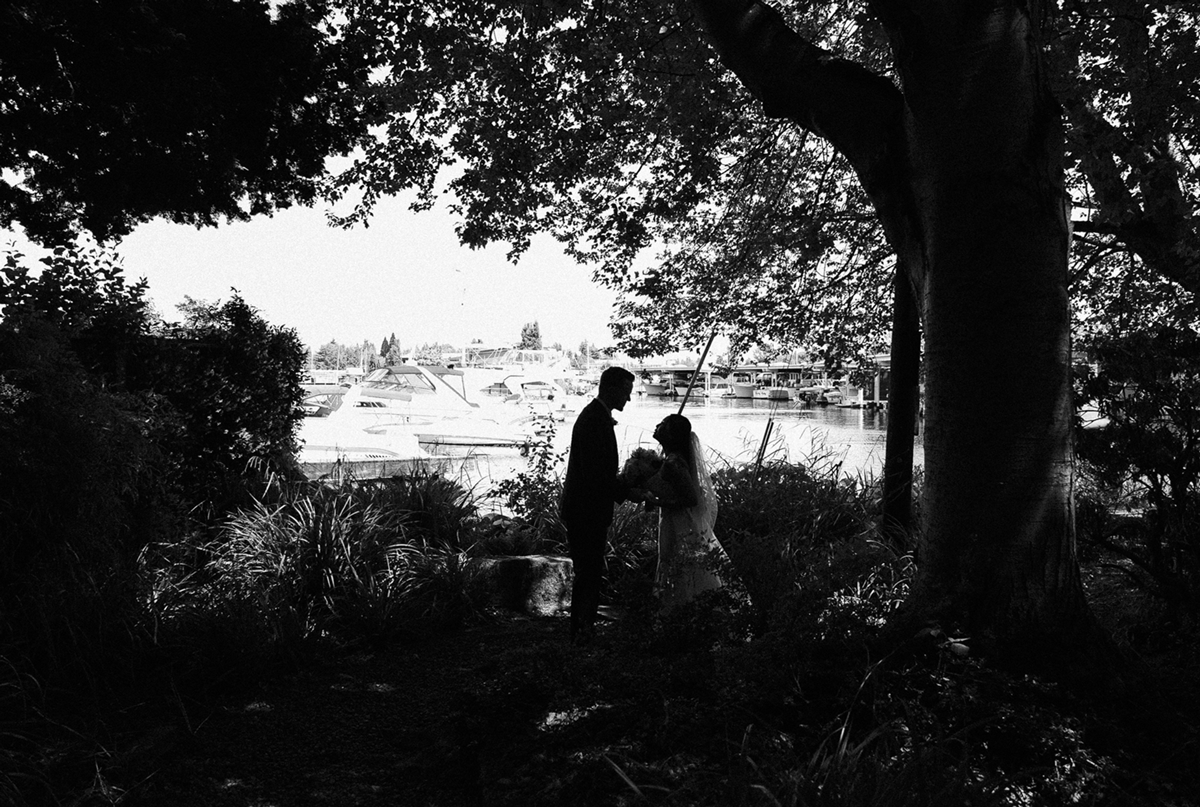 Two silhouetted figures stand beneath a tree overlooking a distant cityscape in black and white.