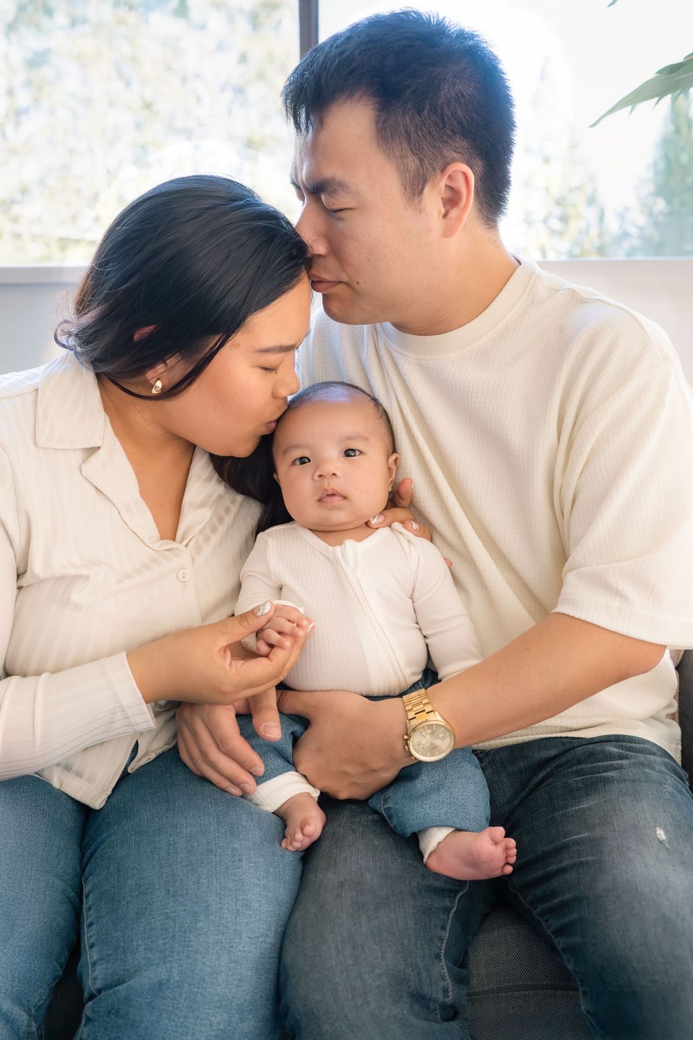 A tender family moment as parents cuddle with their baby in casual white and beige outfits.