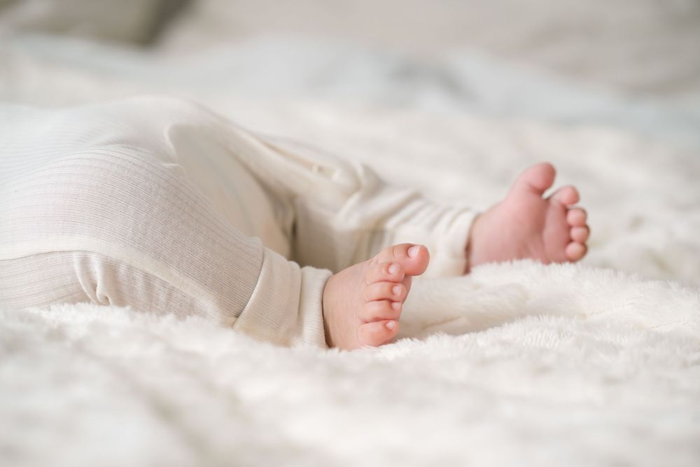 Close-up of tiny baby feet resting on soft white bedding.