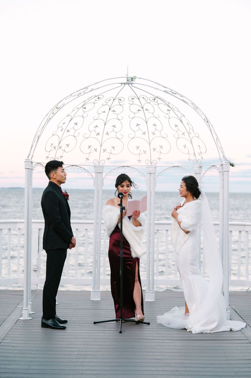 Wedding couple poses under ornate white domed gazebos against a city skyline backdrop.